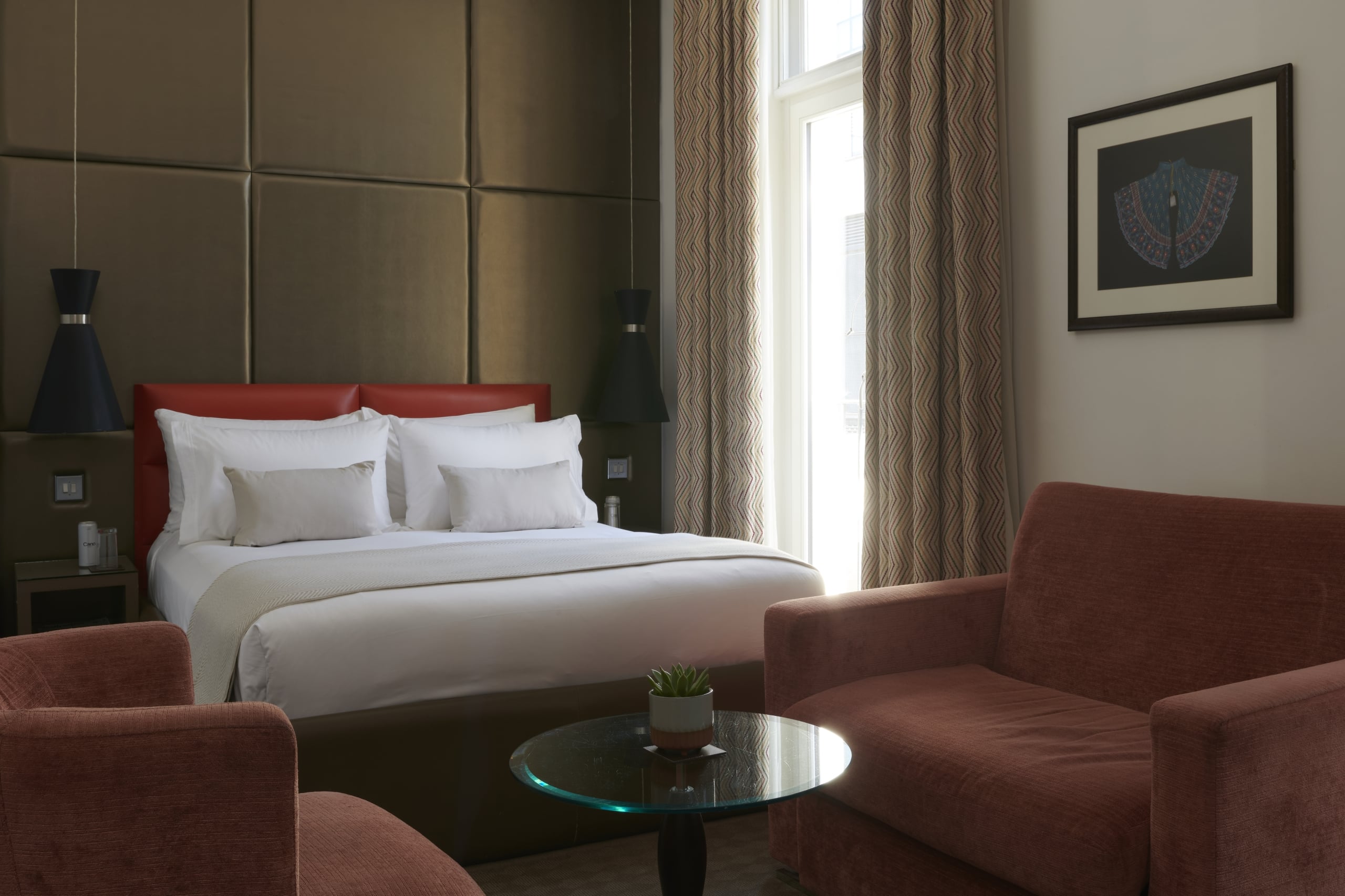 Deluxe Premium King accommodation with red leather headboard, white bedding, two wide armchairs, glass coffee table, and framed artwork.
