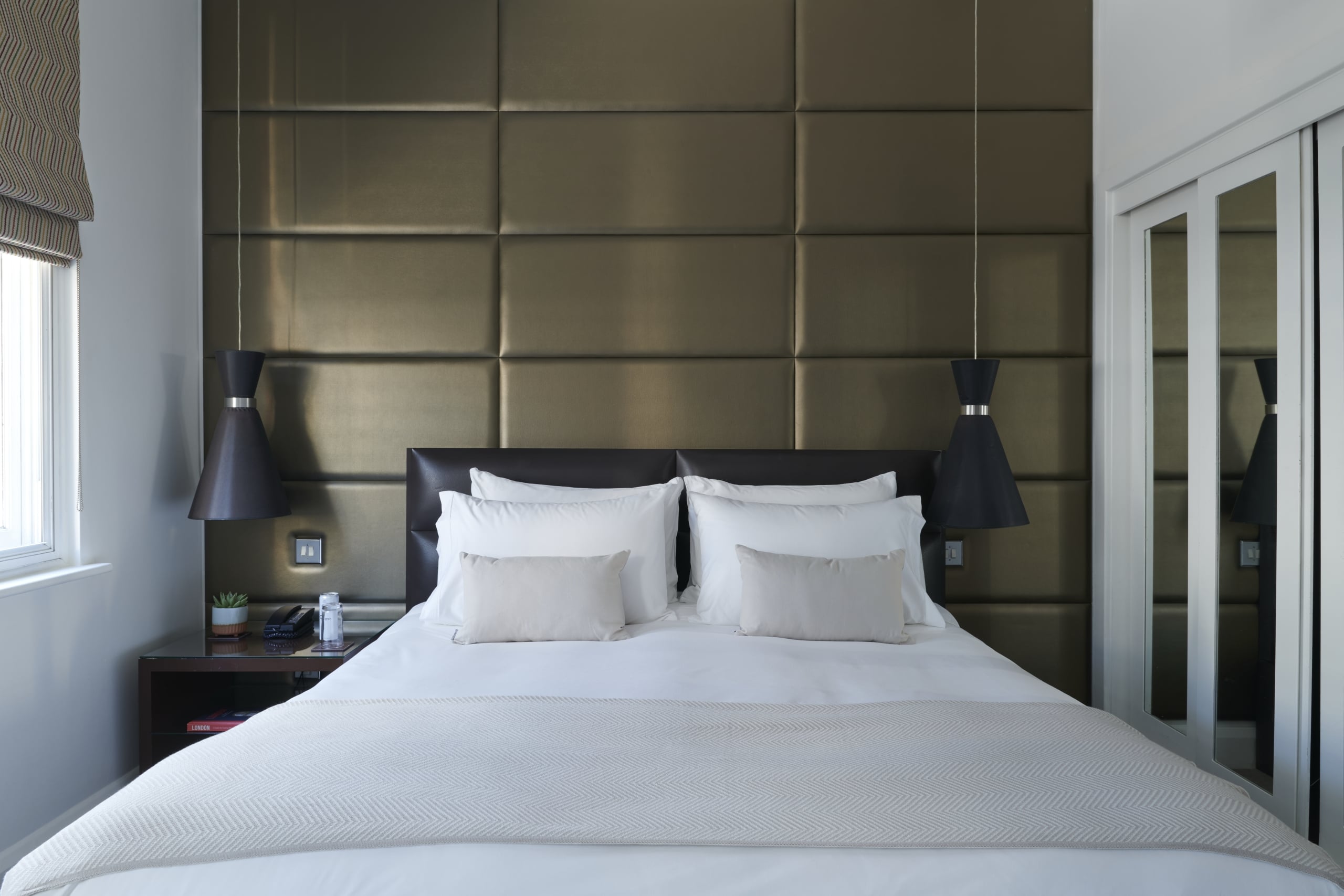 Premium King accommodation with padded wall panel, white bedding, black pendant lights, and mirrored wardrobe.