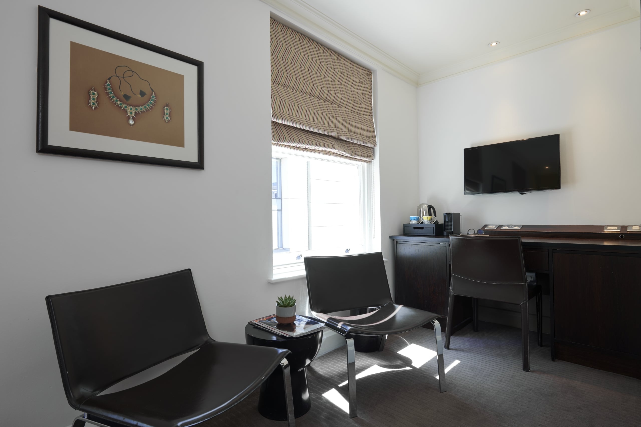Premium King accommodation sitting area with a small kitchenette, wall mounted TV, work desk, and black leather chairs.