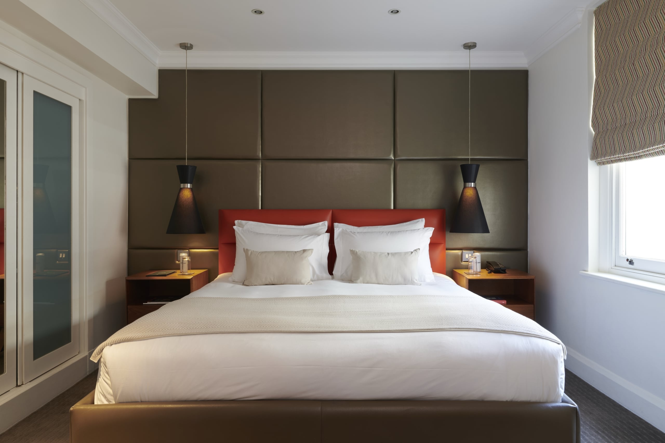 Deluxe Premium King accommodation with red leather headboard, white bedding, hanging pendant lights, and floating night stands.