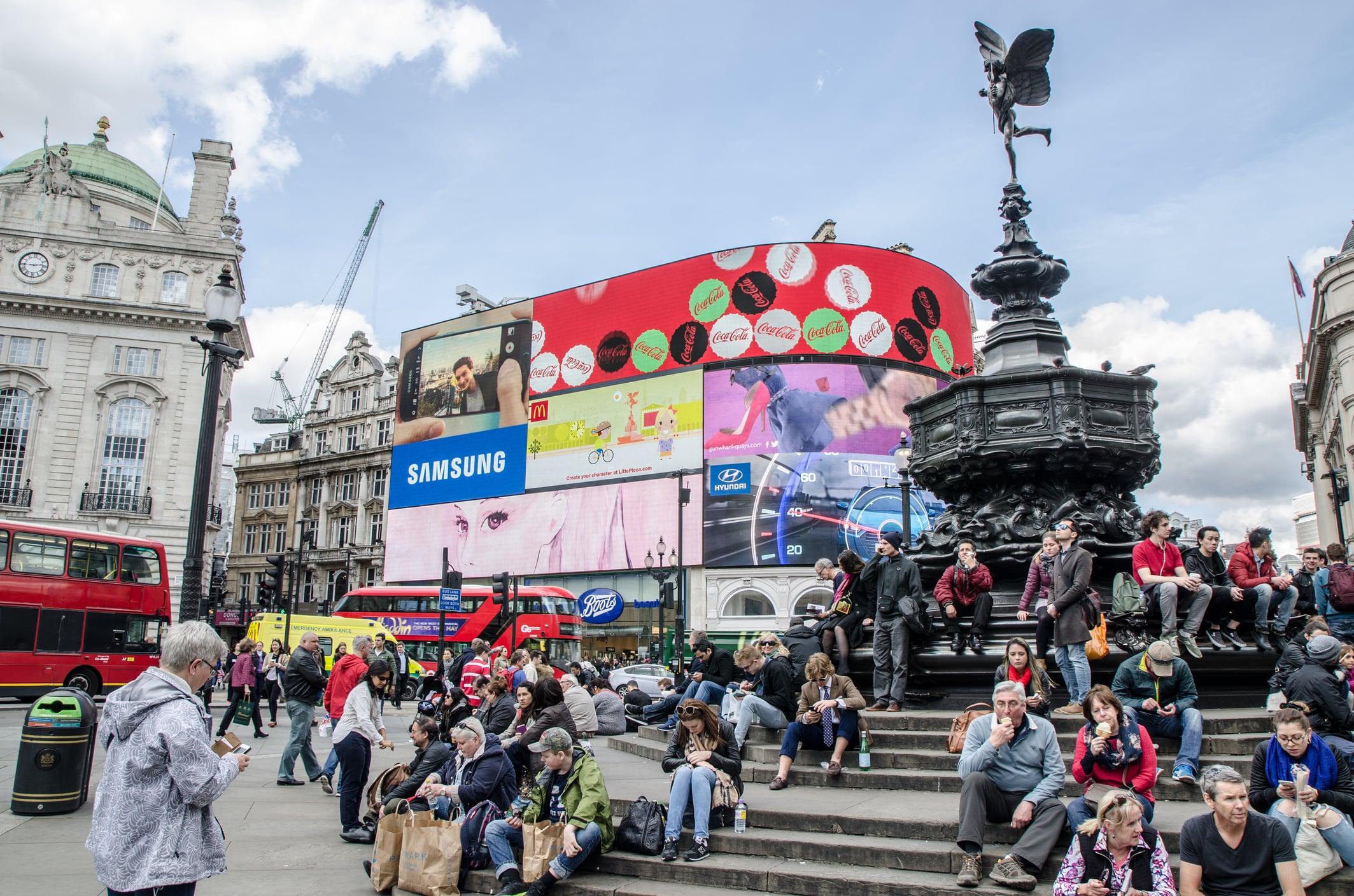 People crossing street and sit on steps of monument at Piccadilly Circus Street in London during daytime