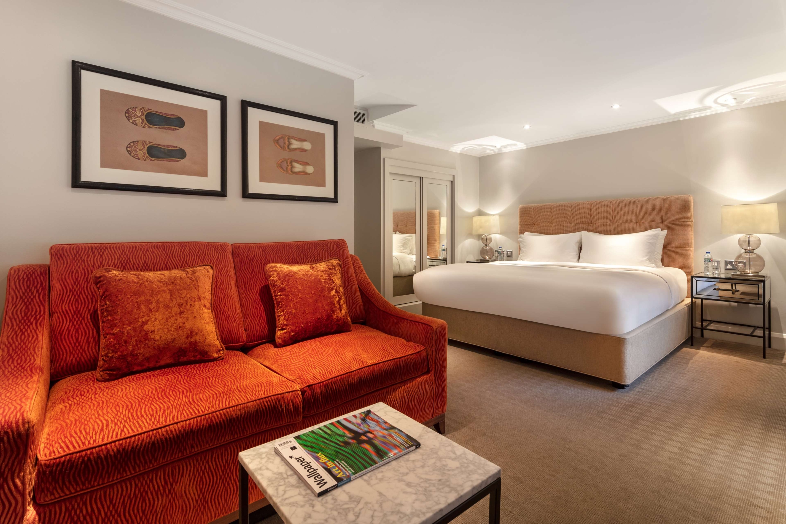 Junior Suite with burnt-orange velvet sofa, tufted headboard over a king bed, marble coffee table, and framed artwork.