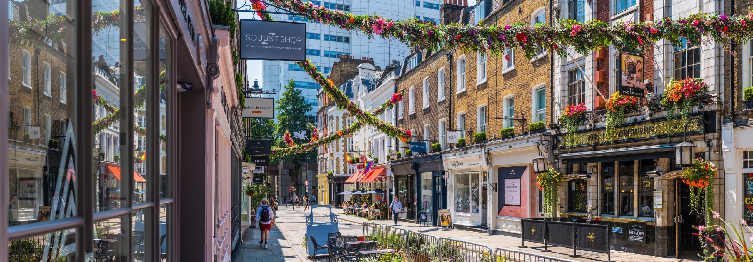 Flower garlands decorating a pedestrianized shopping street of independent stores in Covent Garden Soho, London, UK.